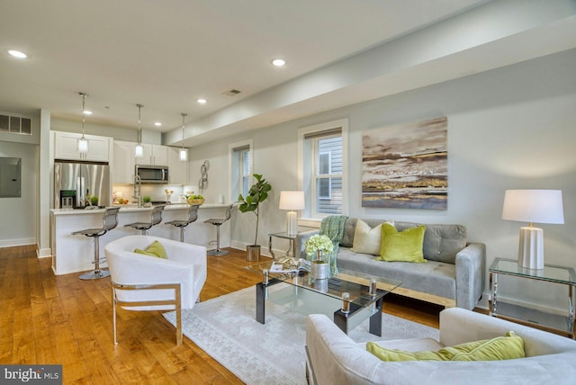 living room with recessed lighting, light wood finished floors, baseboards, and electric panel