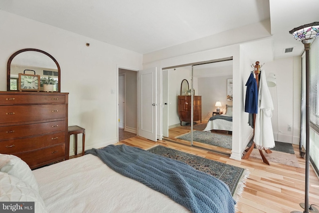 bedroom with light wood-style floors, baseboards, visible vents, and a closet