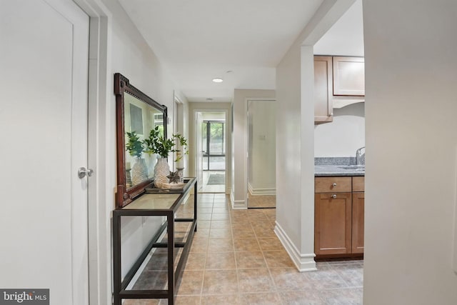 hall featuring baseboards, a sink, and light tile patterned floors