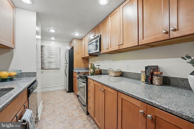 kitchen with dark stone countertops, stainless steel appliances, baseboards, recessed lighting, and light tile patterned floors