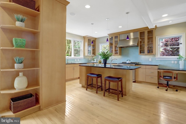 kitchen with dark countertops, a breakfast bar area, wall chimney exhaust hood, a sink, and light wood-style flooring