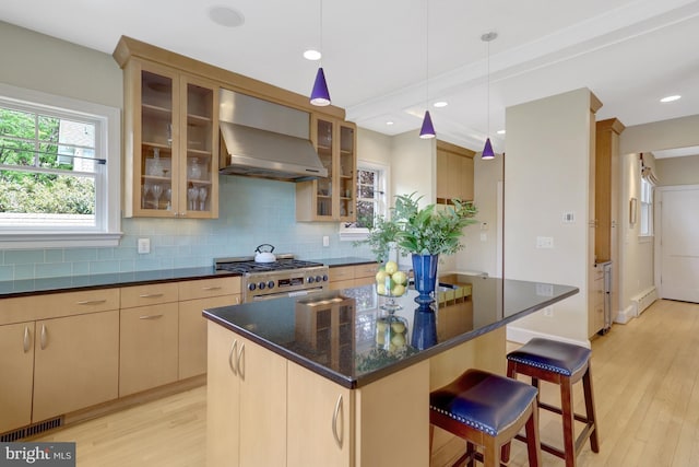 kitchen with light wood finished floors, a breakfast bar area, wall chimney exhaust hood, decorative backsplash, and gas range