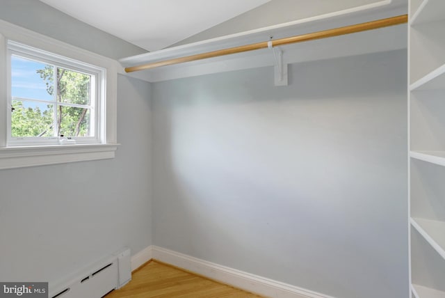 spacious closet with a baseboard heating unit, light wood-style flooring, and lofted ceiling