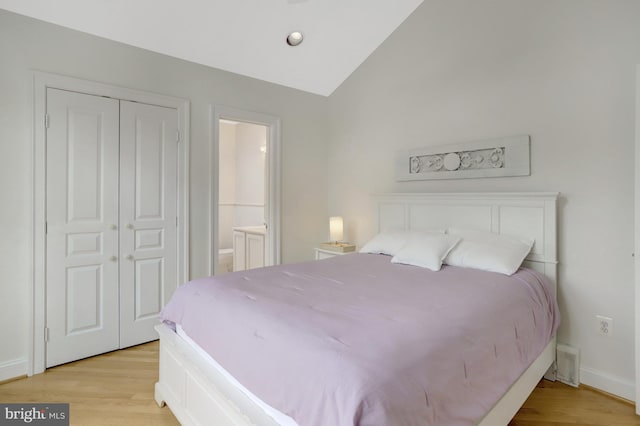 bedroom featuring vaulted ceiling, light wood-type flooring, baseboards, a closet, and connected bathroom