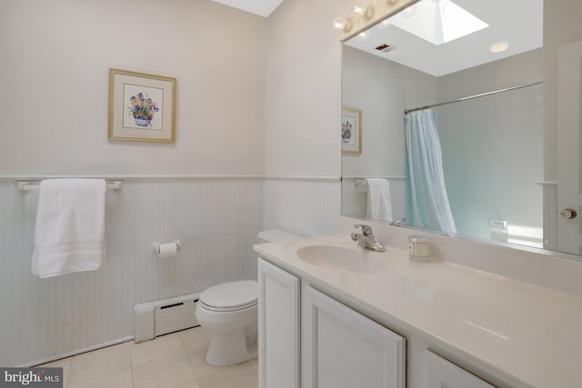 full bath with tile patterned flooring, wainscoting, toilet, baseboard heating, and a skylight
