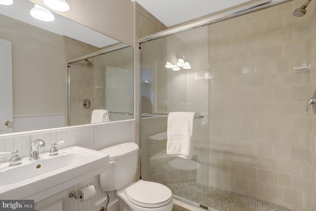 bathroom featuring toilet, wainscoting, a sink, and a stall shower
