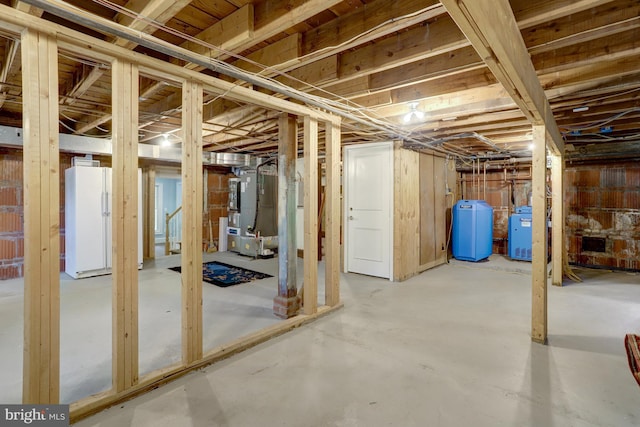 unfinished below grade area featuring freestanding refrigerator and heating unit