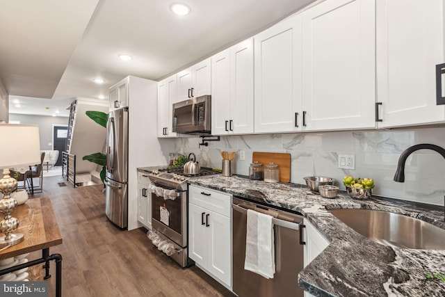 kitchen with a sink, white cabinets, dark stone countertops, stainless steel appliances, and dark wood-type flooring