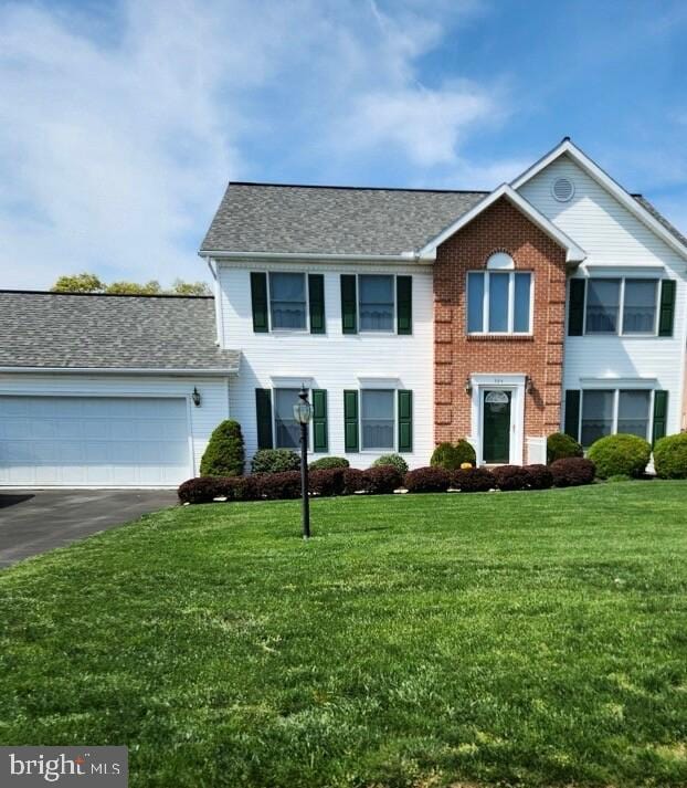 colonial inspired home featuring a front lawn, driveway, a garage, and roof with shingles