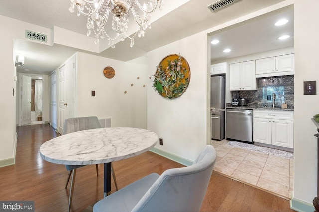 dining area with visible vents, light wood-style floors, baseboards, and an inviting chandelier