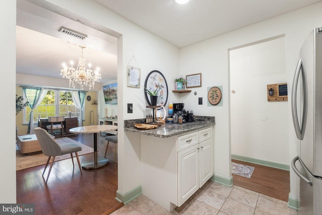 kitchen with a notable chandelier, dark stone countertops, freestanding refrigerator, white cabinetry, and visible vents
