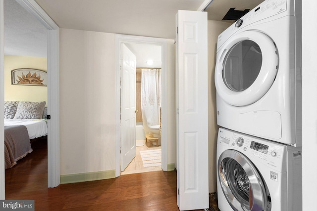 clothes washing area with baseboards, stacked washer and clothes dryer, dark wood-style floors, and laundry area