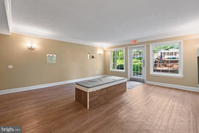 unfurnished living room with a textured ceiling, ornamental molding, baseboards, and wood finished floors