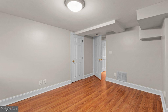 finished basement with baseboards, visible vents, and light wood-style flooring