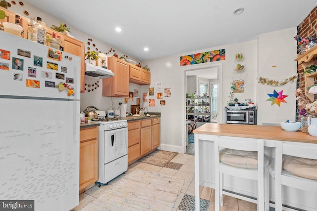 kitchen with recessed lighting, white appliances, light brown cabinets, under cabinet range hood, and dark countertops