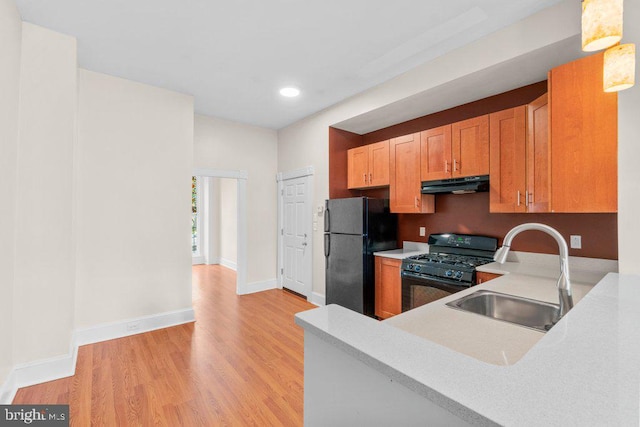kitchen featuring a sink, under cabinet range hood, light wood-type flooring, black appliances, and light countertops