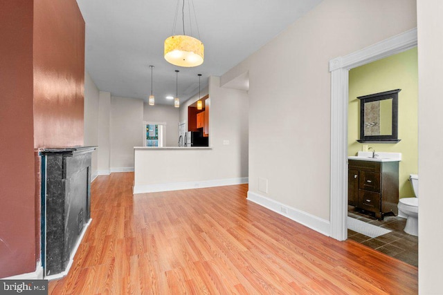 unfurnished living room featuring a sink, baseboards, and light wood-style floors