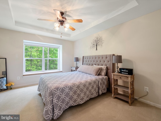 carpeted bedroom featuring a tray ceiling, baseboards, and ceiling fan