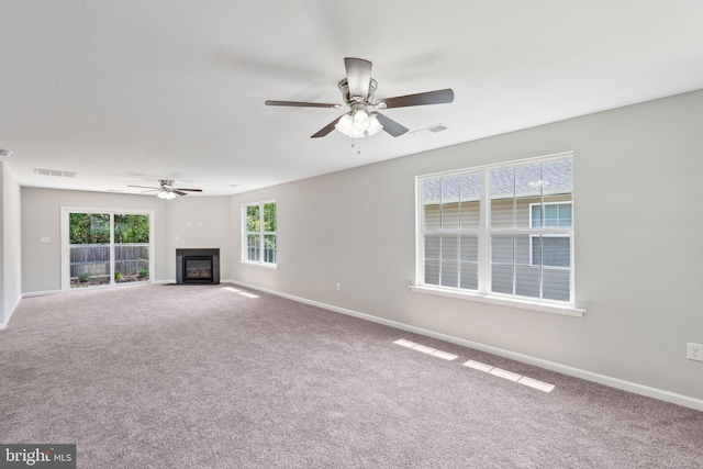 unfurnished living room with ceiling fan, carpet flooring, baseboards, and a glass covered fireplace