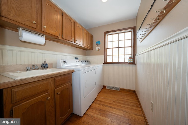 clothes washing area with visible vents, washer and clothes dryer, a wainscoted wall, a sink, and cabinet space