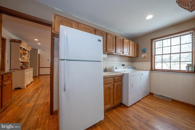 washroom featuring light wood-style floors, a wainscoted wall, washer and dryer, and visible vents