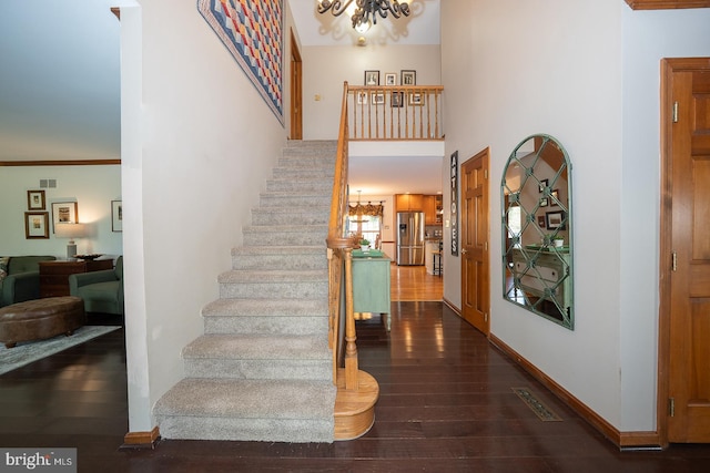 staircase with a towering ceiling, visible vents, hardwood / wood-style flooring, and a notable chandelier