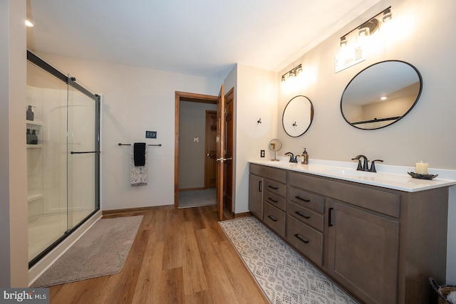 full bath featuring double vanity, a sink, wood finished floors, and a stall shower