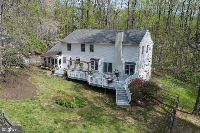 back of house featuring a chimney, roof with shingles, a lawn, a deck, and a wooded view