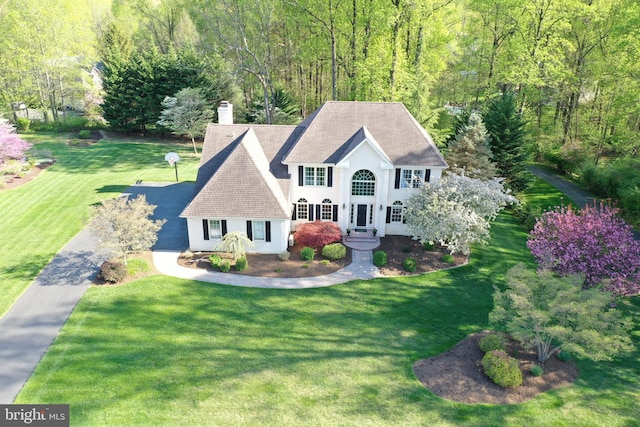 view of front facade with a chimney, stucco siding, a wooded view, roof with shingles, and a front lawn