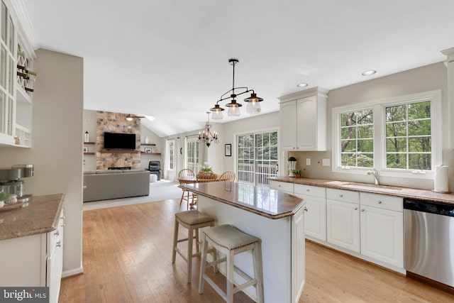kitchen featuring a sink, light wood-type flooring, a breakfast bar, a stone fireplace, and stainless steel dishwasher