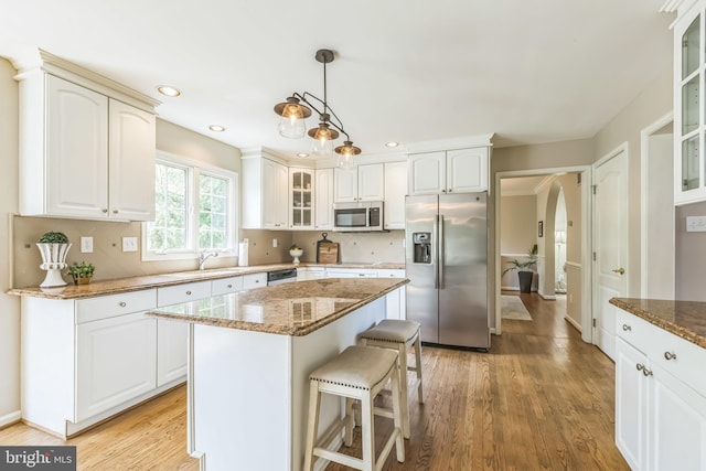 kitchen with dark stone countertops, a breakfast bar area, glass insert cabinets, appliances with stainless steel finishes, and light wood finished floors