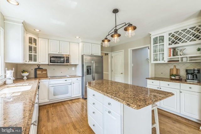kitchen with light wood-style flooring, appliances with stainless steel finishes, backsplash, a sink, and white cabinetry
