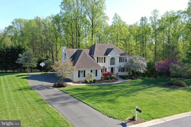 view of front of property featuring stucco siding, a chimney, aphalt driveway, and a front lawn