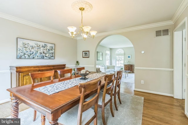 dining room with arched walkways, light wood-style flooring, a chandelier, visible vents, and crown molding