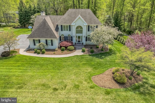colonial home featuring a front lawn, stucco siding, and roof with shingles