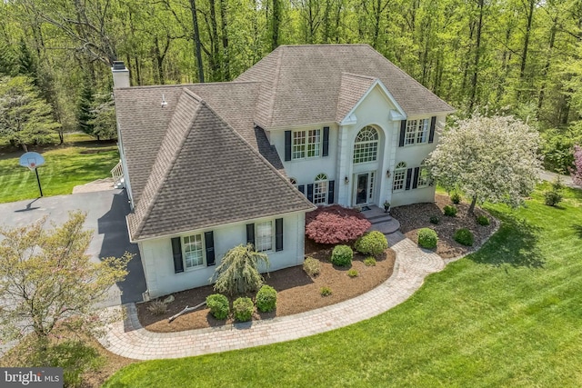 view of front of house featuring a front lawn, a chimney, stucco siding, and roof with shingles
