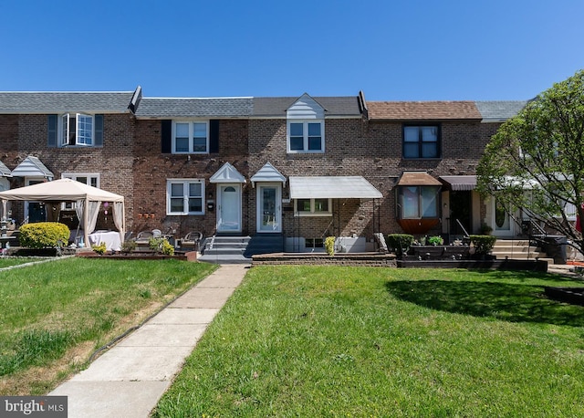 view of property with a gazebo, a front yard, and brick siding