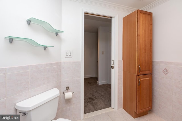 bathroom with tile patterned flooring, crown molding, toilet, tile walls, and a wainscoted wall