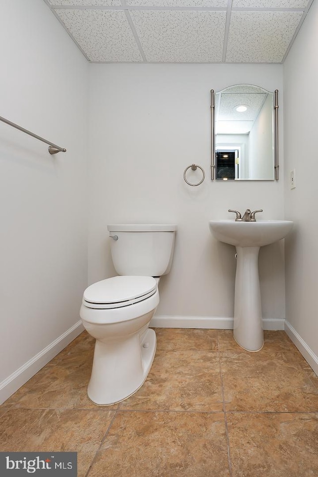 half bathroom with baseboards, toilet, and a paneled ceiling