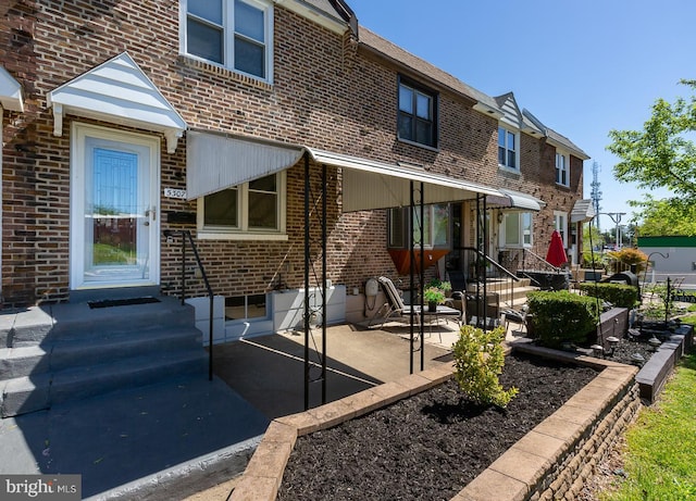 rear view of house with brick siding, entry steps, and a patio