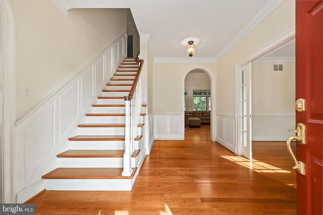 foyer entrance featuring visible vents, arched walkways, light wood-type flooring, ornamental molding, and stairs
