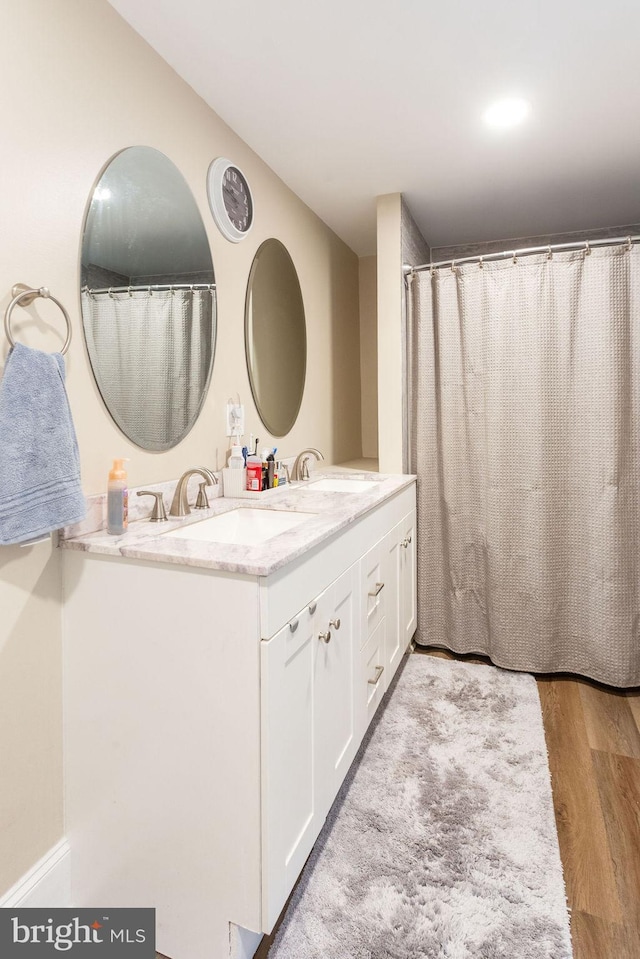 full bath with double vanity, wood finished floors, and a sink