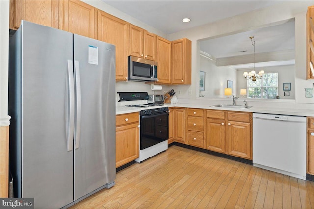 kitchen with appliances with stainless steel finishes, a sink, light countertops, light wood finished floors, and a notable chandelier