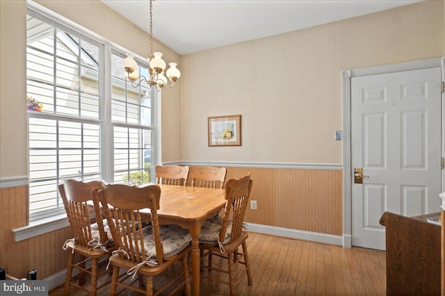 dining space featuring wood walls, a wainscoted wall, a notable chandelier, and hardwood / wood-style floors