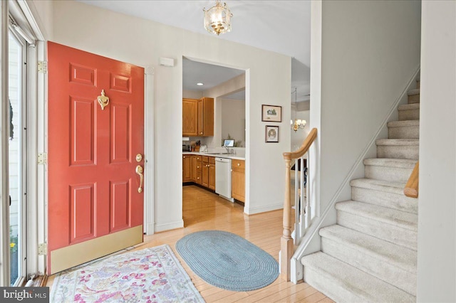 foyer entrance featuring stairs, baseboards, a notable chandelier, and light wood-type flooring