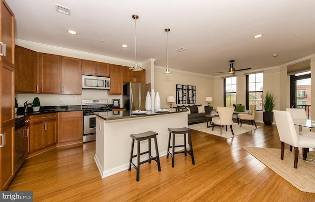 kitchen with visible vents, ornamental molding, a breakfast bar, stainless steel appliances, and light wood-style flooring
