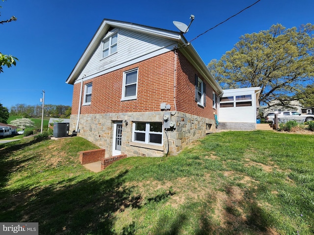 rear view of house featuring central AC, brick siding, and a lawn
