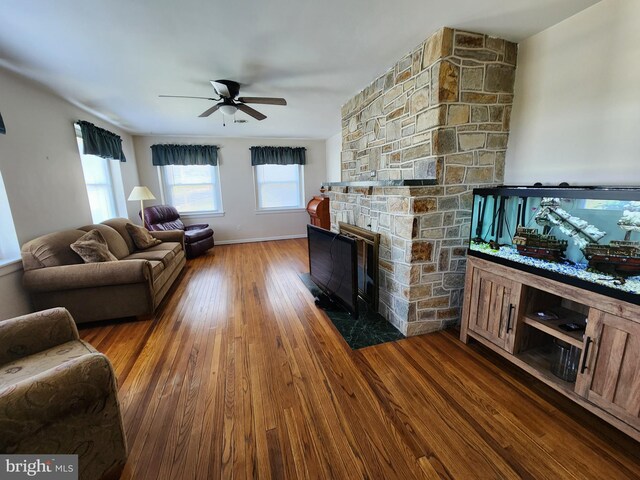 living room with a stone fireplace, ceiling fan, a wealth of natural light, and wood finished floors