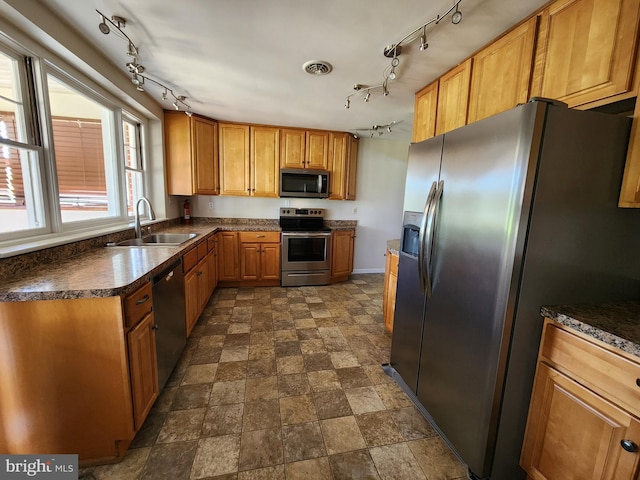kitchen featuring dark countertops, a sink, rail lighting, and appliances with stainless steel finishes