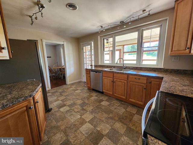 kitchen with stone finish floor, a sink, dark countertops, stainless steel appliances, and track lighting